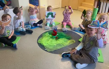 Kita-Kinder sitzen um den Teppich mit der Raupe Nimmersatt